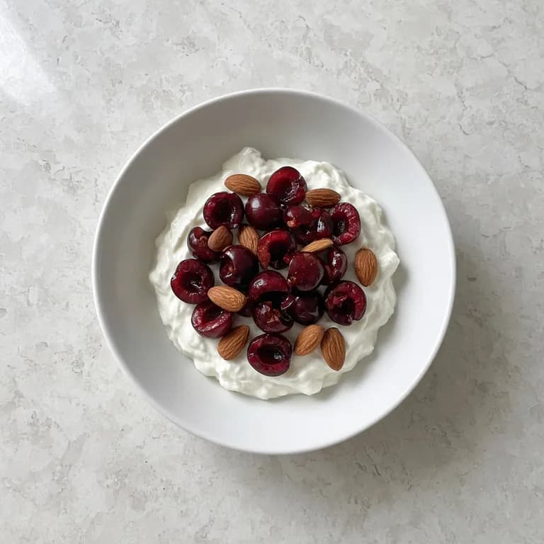 White bowl of skyr topped with halved cherries and chopped almonds.