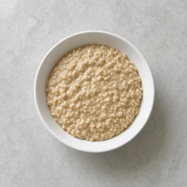 White bowl of creamy oatmeal with a light swirl of heavy cream on top.