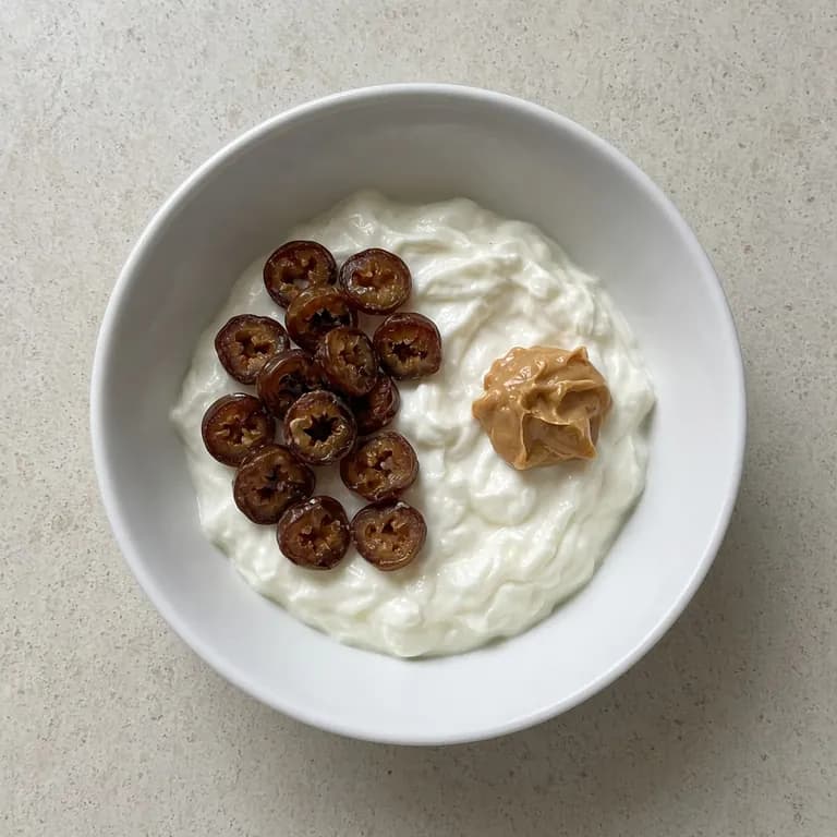 White bowl of thick skyr topped with sliced dates and a spoon of peanut butter.