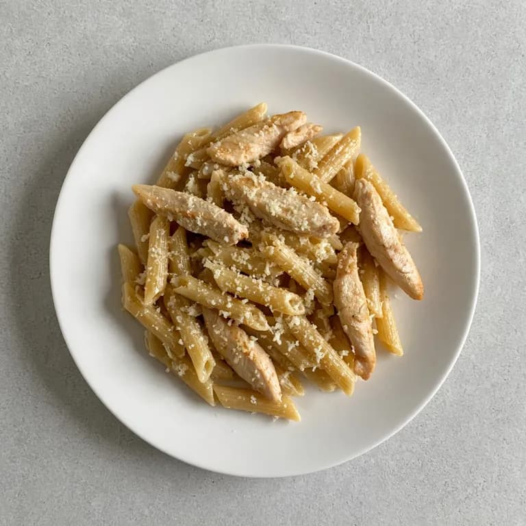 White plate of penne pasta tossed with sliced chicken breast, garlic, olive oil, and grated parmesan.